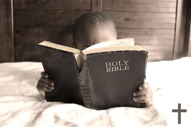boy reading Bible on bed